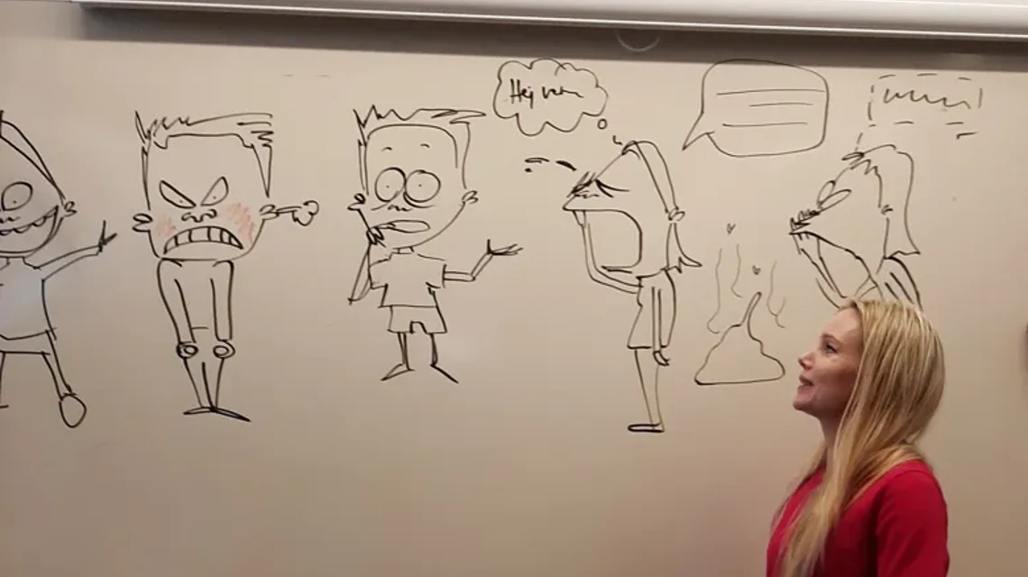 Ung kvinna i röd tröja står framför en whiteboardtavla med tecknade figurer
