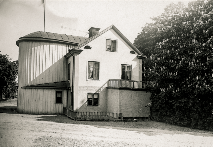 Foto i svart vitt på ett hus med syrenbuskar intill husknuten